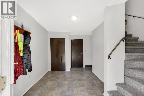 Interior entryway with gray tiled floor, coat rack, two dark wood doors, and stairs. - 38319 Westway Avenue, Squamish