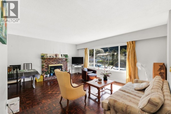 Living room with brick fireplace, dining table, sofa, armchair, and a large window view. - 38319 Westway Avenue, Squamish