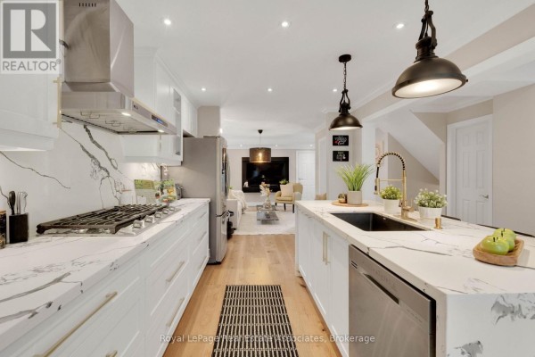Modern kitchen with white cabinetry, marble countertops, stainless steel appliances, and light wood floors. - 3840 Althorpe Circle, Mississauga