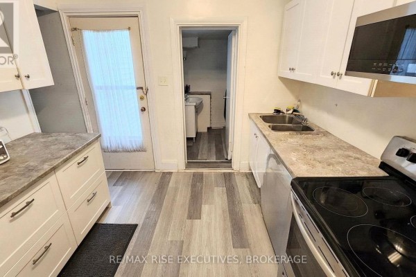 Kitchen with white cabinets, grey laminate flooring, double sink, and a doorway to laundry. - 385 Alfred Street, Kingston