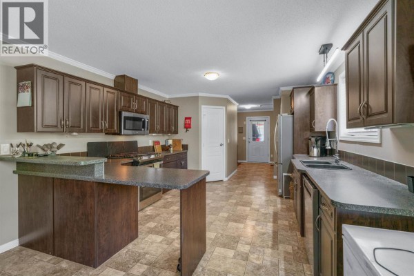 Kitchen area of a mobile home with dark wood cabinets, granite countertops, stainless steel appliances, and tile flooring. - 385 Colgrove Road, Hixon