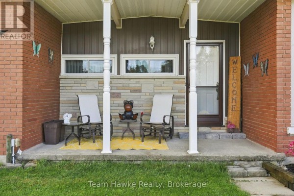 Covered front porch with seating, stone accent wall, and decorative butterflies on the brick facade. - 385 Lafontaine Road W, Tiny