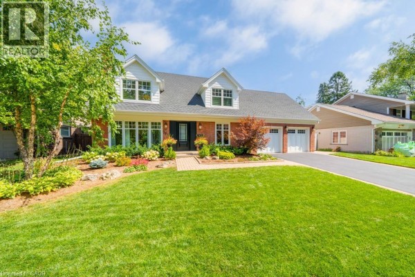 Side view of a brick house with a double garage, surrounded by lush greenery and a paved driveway. - 385 Rosslyn Drive, Burlington