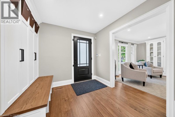 Entrance foyer with hardwood floors, a black front door, and white built-in storage with a wooden bench. - 385 Rosslyn Drive, Burlington