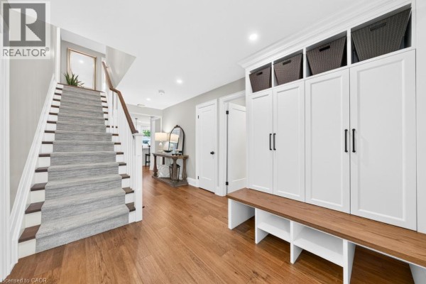 Hallway with hardwood floors, a staircase with grey carpet runner, and white built-in storage with a wooden bench. - 385 Rosslyn Drive, Burlington