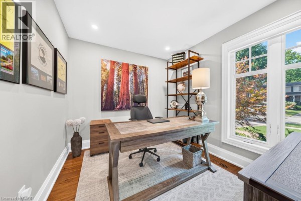 Home office with a large window, wooden desk, chair, shelving unit, and artwork of redwood trees. - 385 Rosslyn Drive, Burlington