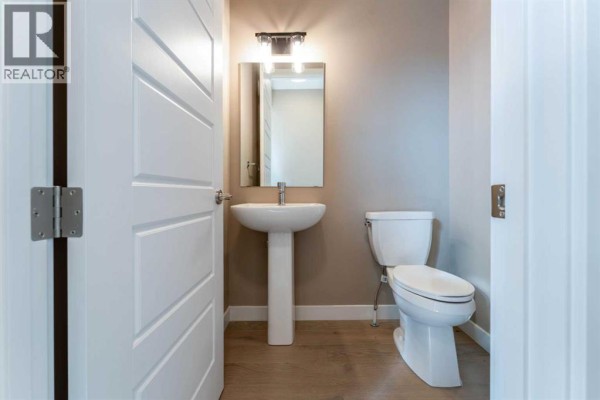 Small powder room with white pedestal sink, toilet, and a modern vanity light. - 385 Waterford Boulevard, Chestermere