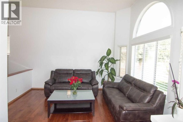 Living room with two brown leather sofas, a dark wood coffee table, and wood flooring. - 3850 Catalina Boulevard Ne, Calgary