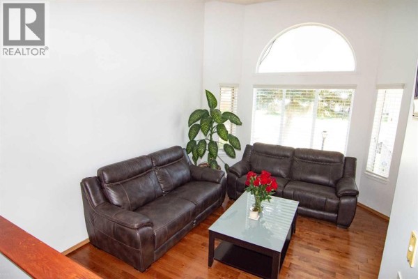 Living room with two brown leather sofas, a dark wood coffee table, and large arched windows. - 3850 Catalina Boulevard Ne, Calgary