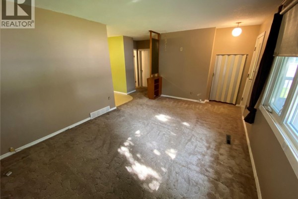Spacious living room with beige carpet, a room divider, and a window with dark curtains. - 386 4th Avenue N, Yorkton