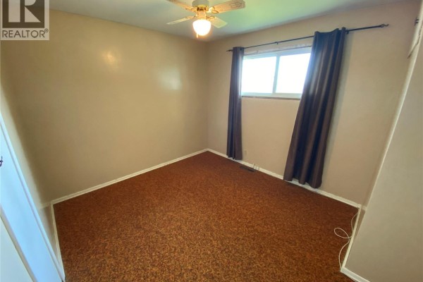Bedroom with brown speckled carpet, tan walls, and a ceiling fan with a light. - 386 4th Avenue N, Yorkton