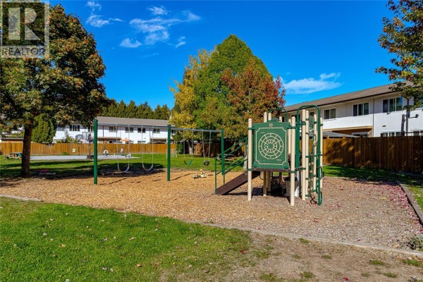 Community playground with swings and a green climbing structure on wood chip ground. - 386 Burnside Rd W, Saanich