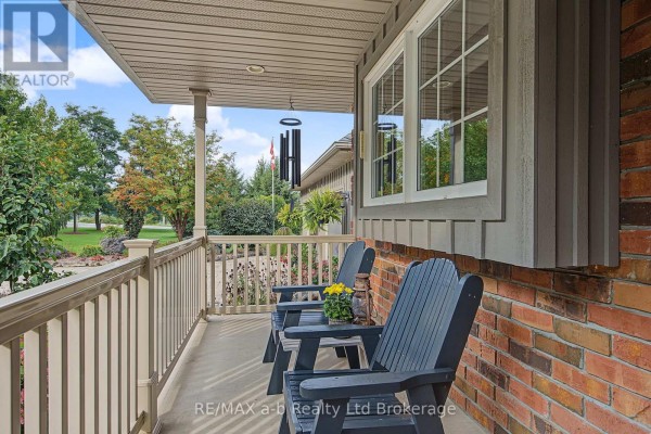 Close-up of a covered front porch with two dark Adirondack chairs, a small table, and a brick exterior. - 386087 Second Road, Norwich