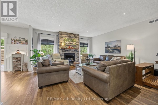 Living room with a stone fireplace, leather sofas, hardwood floors, and large windows overlooking the outdoors. - 386087 Second Road, Norwich