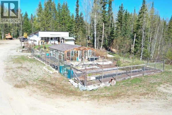 Side view of the workshop showing attached blue shipping container and surrounding dirt yard with vehicles. - 3865 Blue Ridge Road, Quesnel