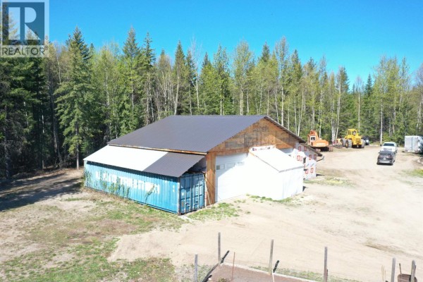 View of a greenhouse and raised garden beds in front of the workshop with surrounding trees. - 3865 Blue Ridge Road, Quesnel