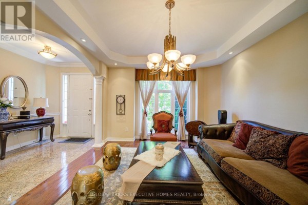 Living room with a tray ceiling, chandelier, brown sofa, ornate coffee table, and arched entryway. - 3885 Eglinton Avenue, Mississauga