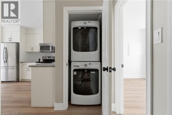 Stacked white washer and dryer in a closet with a dark wooden door frame. - 389 Dundas Street, Woodstock