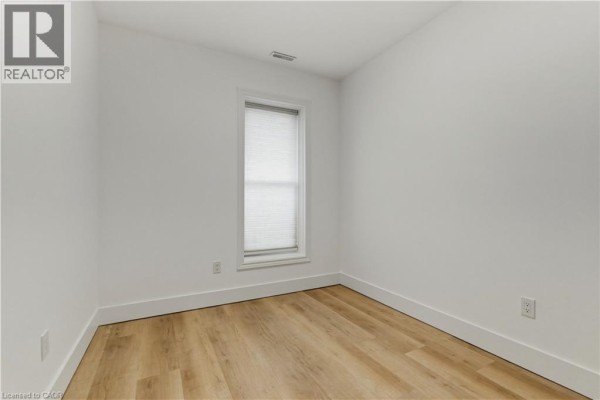 Small, empty room with white walls, light wood floors, and a single window with blinds. - 389 Dundas Street, Woodstock