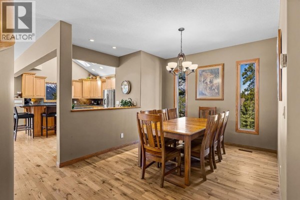 Dining room with a wooden table, chairs, and large windows overlooking trees. - 389 Eagle Heights, Canmore