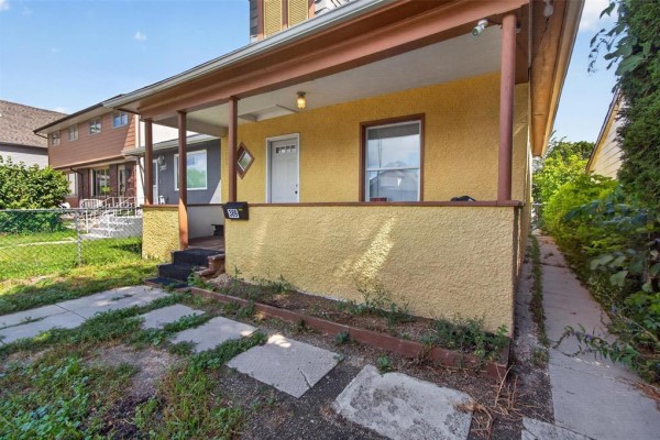 Side view of the yellow house exterior showing the porch and driveway. - 389 Harbison Avenue W, Winnipeg