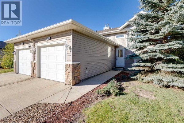 Close-up of the duplex exterior with a double garage, beige siding, and decorative stone. - 389 Stonegate Way Nw, Airdrie