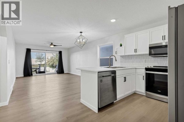 Open concept living and kitchen area with white cabinets, stainless steel appliances, and light wood floors. - 389 Stonegate Way Nw, Airdrie
