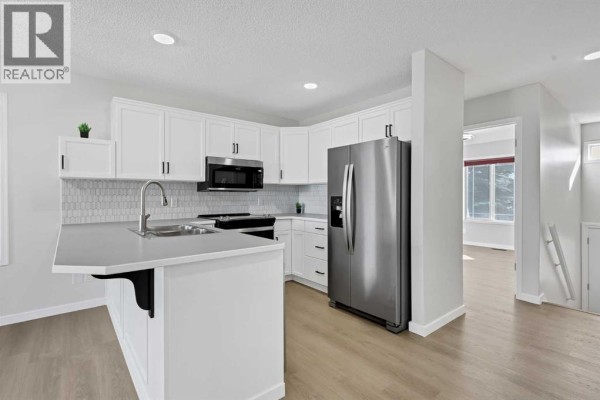 Kitchen with white shaker cabinets, stainless steel appliances, a grey countertop, and a view of a dining area. - 389 Stonegate Way Nw, Airdrie
