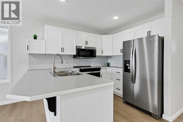 Kitchen with white shaker cabinets, a large stainless steel refrigerator, and a grey countertop island. - 389 Stonegate Way Nw, Airdrie