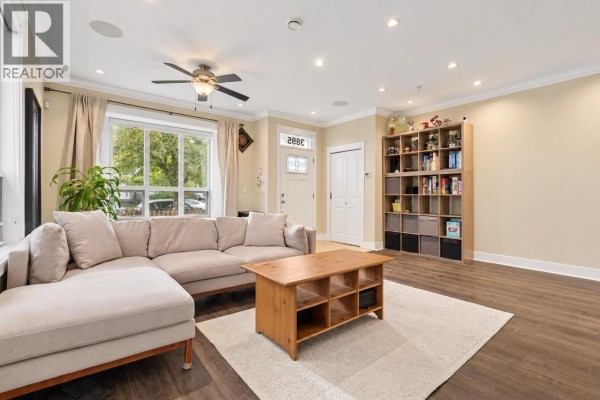 Living room with a sectional sofa, coffee table, and large bookshelf. - 3895 Dumfries Street, Vancouver