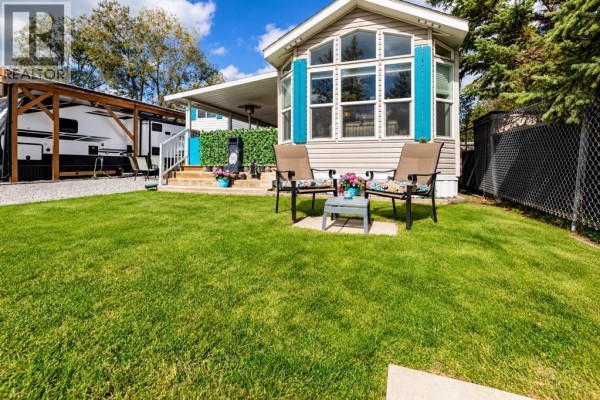 Chairs and a table on a green lawn in front of a beige mobile home with blue shutters. - 39, 12036 Township Road 422, Rural Ponoka County