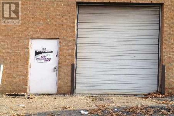 Exterior of a commercial building featuring a white door and a large metal roll-up garage door. - 39 - 14 Automatic Road, Brampton
