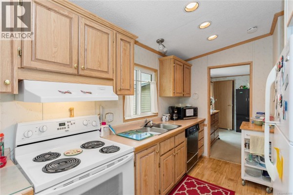 Kitchen with white appliances, light wood cabinets, and a stainless steel double sink. - 39 1048 Murchie Way, Nanaimo