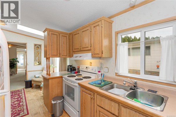 Kitchen counter with sink, window view to adjacent property, and wood cabinets. - 39 1048 Murchie Way, Nanaimo