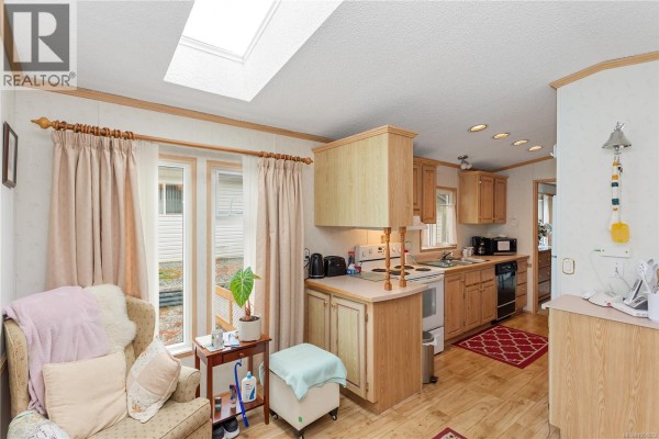Kitchen with light wood cabinets, a skylight, and a sitting area with armchair. - 39 1048 Murchie Way, Nanaimo