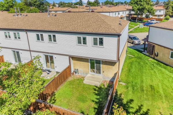 Backyard of a townhouse with a grass lawn, wooden fence, and sliding glass doors. - #39 14511 52 St Nw, Edmonton