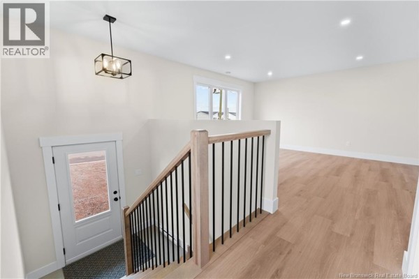 Interior view of a staircase with black spindles and wooden banister, leading to a bright living area. - 39 Alosier Crescent, Moncton