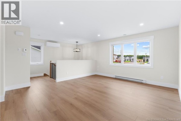 Spacious living room with light wood laminate flooring, white walls, and a large window overlooking the street. - 39 Alosier Crescent, Moncton