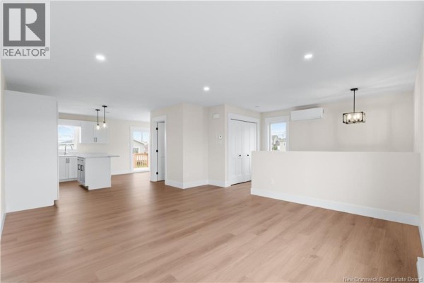 Open-concept living area with light wood floors, white walls, and a view into the kitchen. - 39 Alosier Crescent, Moncton