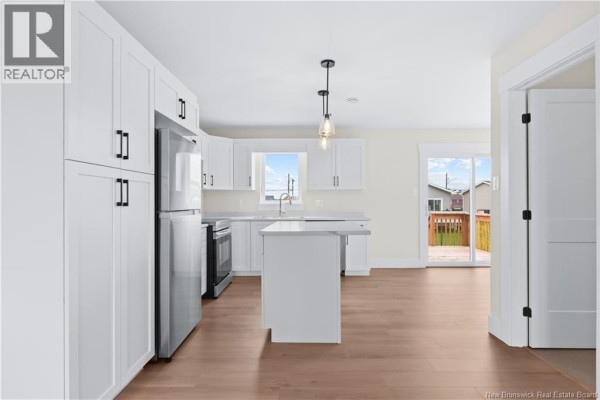 Modern white kitchen with stainless steel appliances, a central island, and a sliding glass door to the exterior. - 39 Alosier Crescent, Moncton