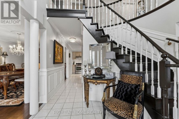 Foyer with white tile floor, dark wood staircase, and view into dining and kitchen areas. - 39 Banner Road, Brampton