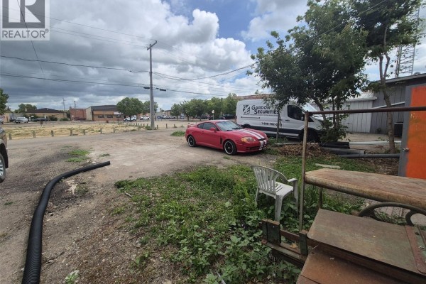 Rear lot with a red car, white van, and various industrial items. - 39 Betts Avenue, Yorkton