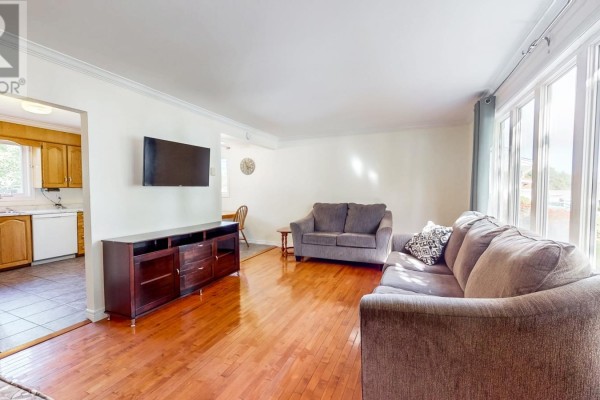 Living room with hardwood floors, grey sofas, a TV, and a view into the kitchen. - 39 Birchwynd Street, St John S