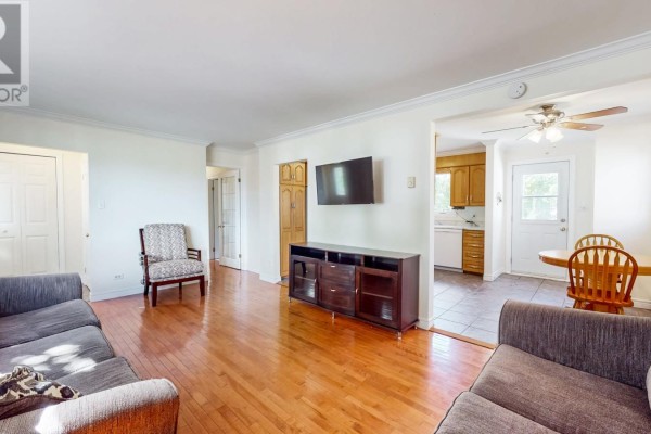Living room with hardwood floors, grey sofas, a TV, and an open doorway to the kitchen. - 39 Birchwynd Street, St John S