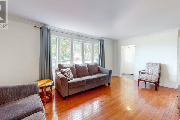 Living room with hardwood floors, grey sofas, a bay window, and a patterned armchair. - 39 Birchwynd Street, St John S