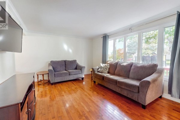 Living room with hardwood floors, two grey sofas, a TV, and a bay window overlooking the exterior. - 39 Birchwynd Street, St John S