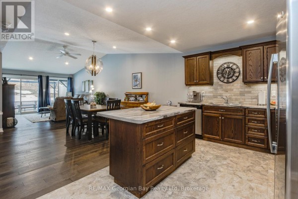 Open-concept living and dining area with dark wood floors, dining table, and a kitchen island with stone countertop. - 39 Chamberlain Crescent, Penetanguishene