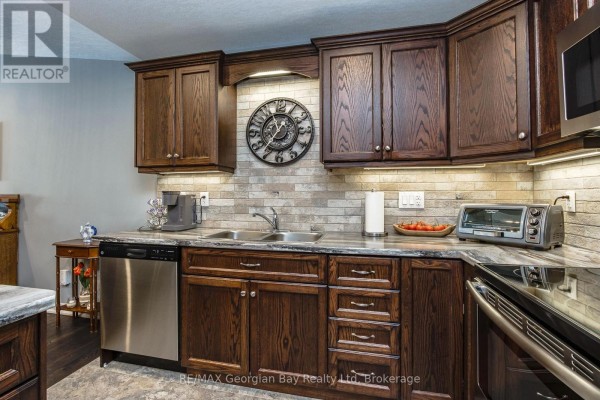 Kitchen with dark wood cabinets, granite countertops, stainless steel dishwasher, and a tiled backsplash with a large clock. - 39 Chamberlain Crescent, Penetanguishene