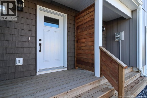 Close-up of a white front door with a window on a townhouse with a wooden porch. - 39 Downsview Drive, Saint John