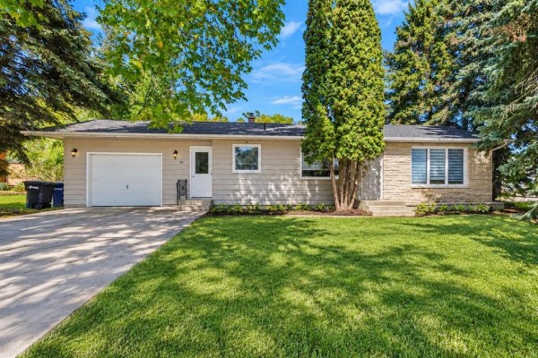 Front view of a light beige bungalow with a stone accent on the right side and a well-kept lawn. - 39 First Avenue N, Blumenort